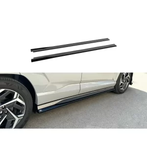 The image is divided into two parts. At the top, two gloss black side skirt extensions are shown individually against a white background. They are long, slim, and straight, designed to be mounted along the lower edges of the vehicle's body. Below, a close-up of the passenger side of the Hyundai Kona N Line shows the skirt extension installed. The part hugs the underside of the vehicle, sitting flush with the lower door panel. Its glossy black finish enhances the car's sporty aesthetic while offering subtle protection from road debris.