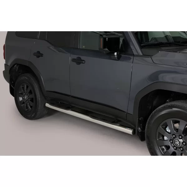 Passenger-side view of a 2025 Toyota Land Cruiser 250 in dark grey, showing compact stainless steel side steps mounted below the doors to assist entry and exit.