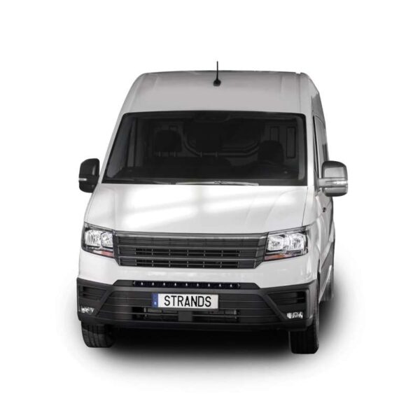 a full-frontal view of a white MAN TGE van parked in a studio environment with a white background. The van has a tall, boxy shape with a wide windshield, dual side mirrors, and a horizontal front grille. Just below the grille, integrated into the black front bumper area, is a slim LED light bar. The bar sits centrally above the license plate, which displays the word "STRANDS." The LED bar adds a sleek, modern touch to the front fascia, providing additional forward lighting for nighttime or off-road driving.