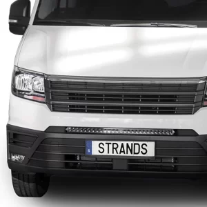 This close-up image focuses on the front center section of the MAN TGE van, highlighting the Dark Knight 30 LED light bar. Positioned just above the license plate and beneath the lower grille, the LED bar spans almost the full width of the plate frame. It consists of a single row of powerful diodes encased in a slim, black housing with a subtle glossy finish. The grille above is made of horizontal black slats, and the vehicle's bumper is sculpted with clean, angular lines. The LED bar’s integration looks factory-fitted, enhancing both visibility and aesthetics.