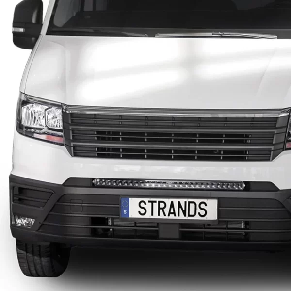 This close-up image focuses on the front center section of the MAN TGE van, highlighting the Dark Knight 30 LED light bar. Positioned just above the license plate and beneath the lower grille, the LED bar spans almost the full width of the plate frame. It consists of a single row of powerful diodes encased in a slim, black housing with a subtle glossy finish. The grille above is made of horizontal black slats, and the vehicle's bumper is sculpted with clean, angular lines. The LED bar’s integration looks factory-fitted, enhancing both visibility and aesthetics.